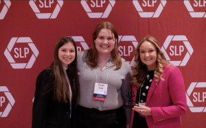 Three woman smiling in front of a red backdrop.